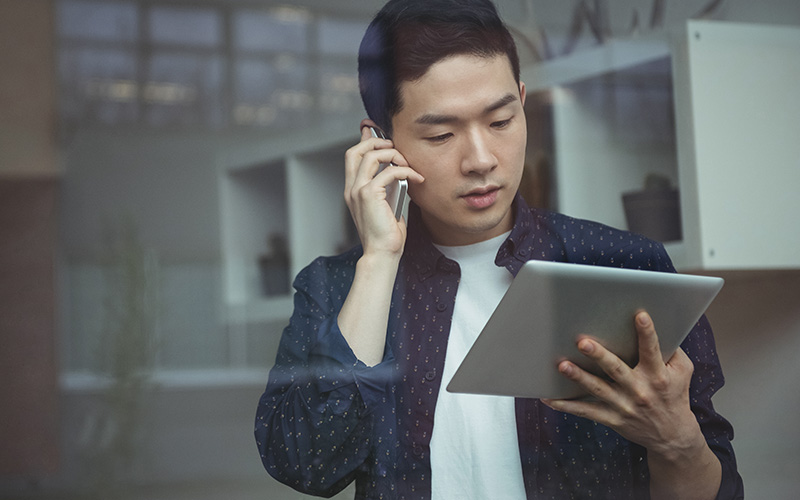 Man working remotely using a tablet while on a phone call, illustrating tech job flexibility.