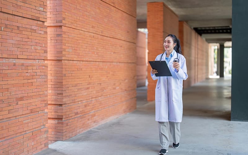 Life science professional in a lab coat walking on campus.