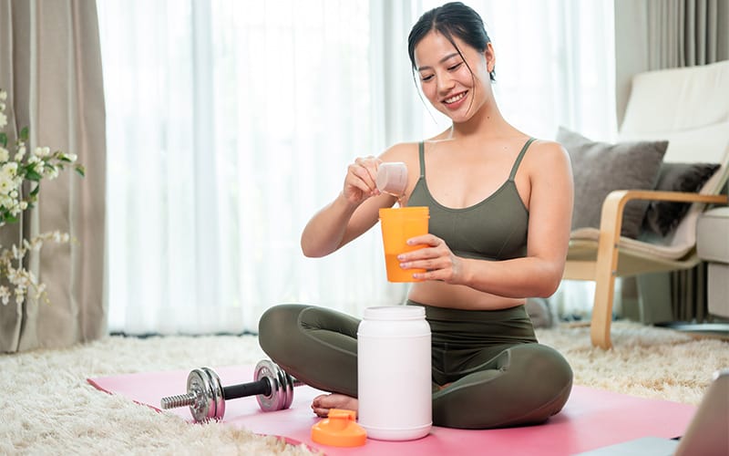 Woman mixing sports supplements into a shaker at home.