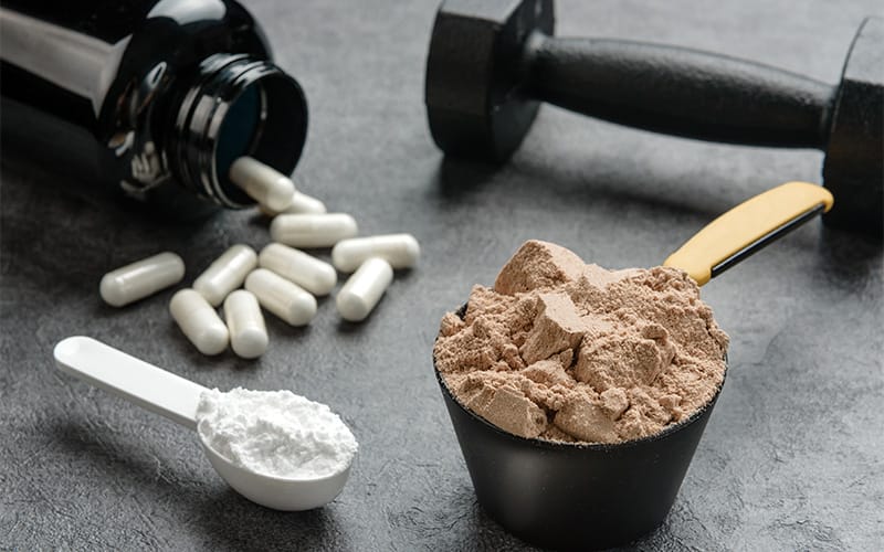Close-up of sports supplements: protein powder, capsules, and creatine.