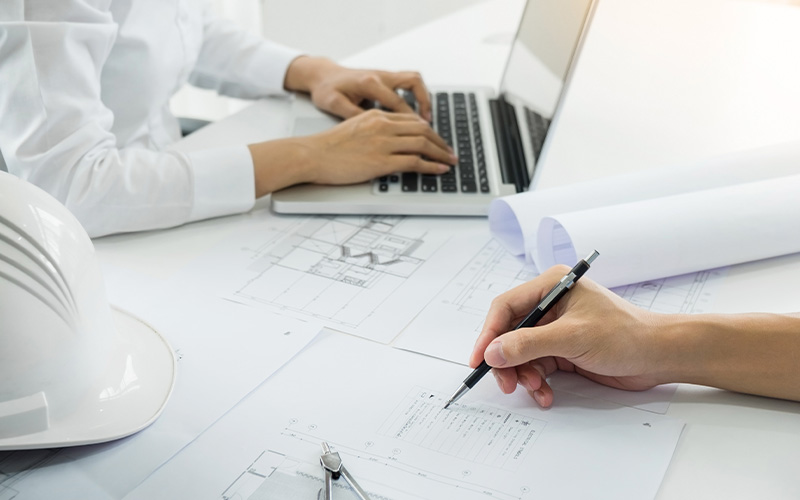 Engineers working on blueprints and a laptop.