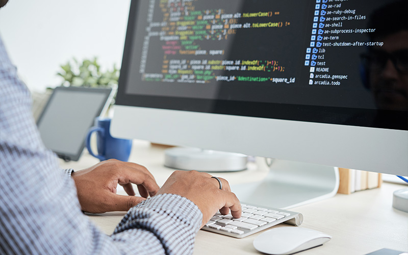 Hands type code on a computer keyboard.