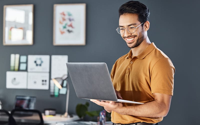 Man smiling while looking at his laptop in an office.