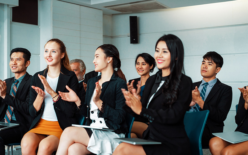 Professionals listening and clapping at an AI workplace seminar.