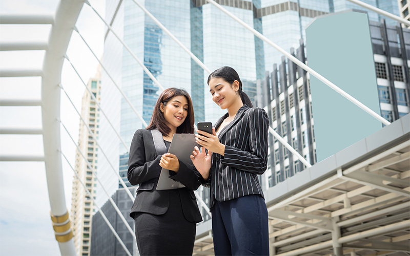 Businesswomen collaborating with a phone and tablet.